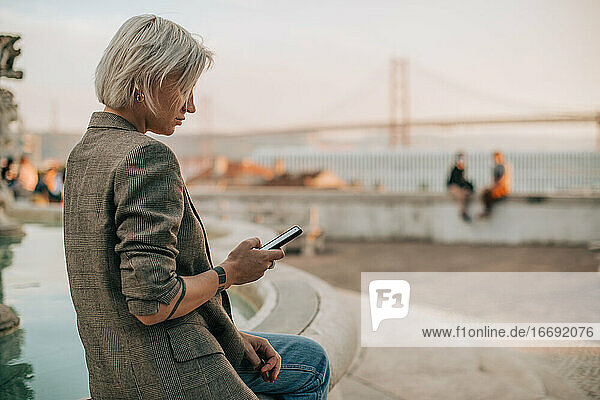 Woman using her smartphone while sitting in the street in the evening