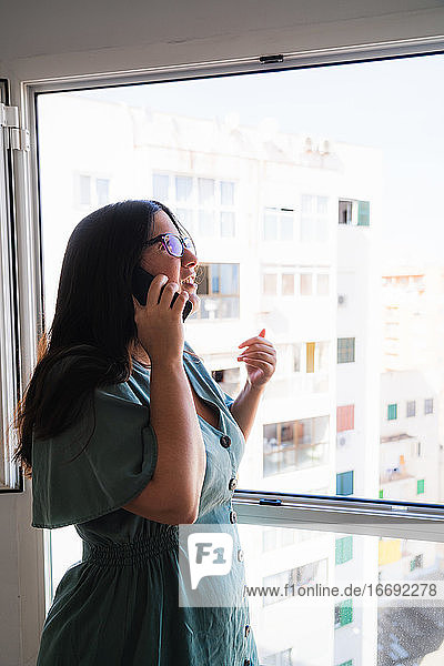 Brünette Spanierin im seriösen Business-Look telefoniert am Fenster ihrer Wohnung am Nachmittag in Palma de Mallorca  Spanien während der Coronavirus-Entbindung