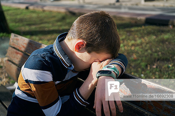child on a bench covers his face with his arm and is crying