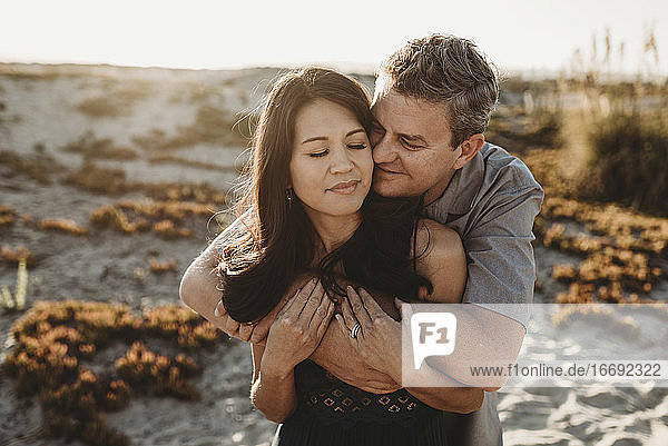 Ehemann Mitte 40 umarmt schöne Frau mit Sanddüne im Hintergrund