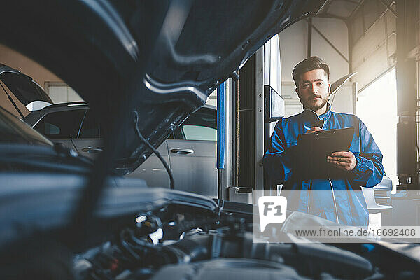Auto mechanic fills in car repair documentation.