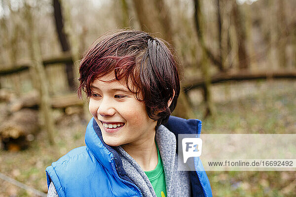 A smiling boy looks off to the side while standing in woods in Spring