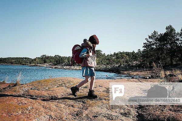 young girl hiking with a backpack on some rocks in Finland by the sea
