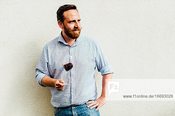 Kaukasischer Mann hält ein Glas Rotwein auf neutralem Hintergrund