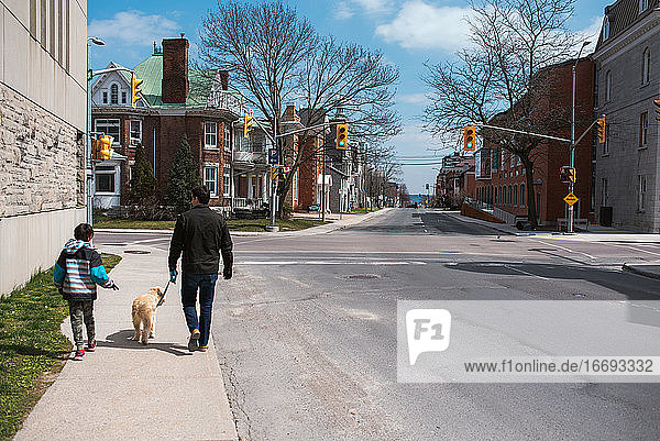 Vater und Sohn gehen mit ihrem Hund auf dem Bürgersteig einer ruhigen Stadtstraße spazieren.