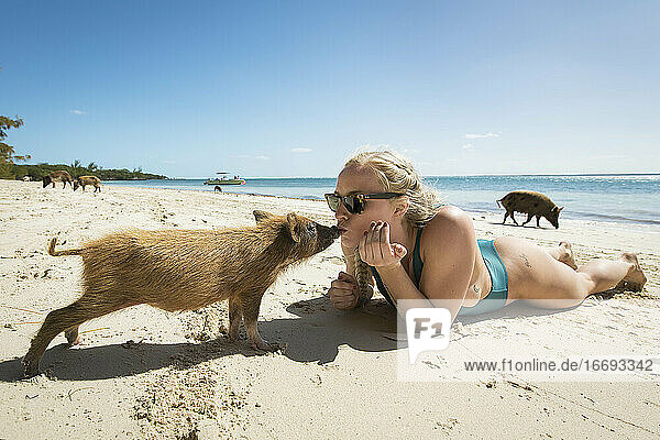 Young woman kissing piglet while lying on sand at beach during summer vacation