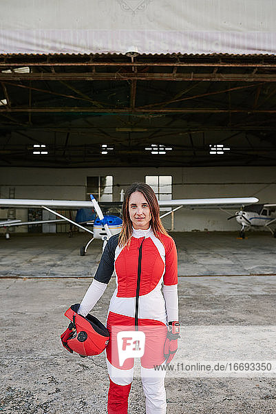 Junge Fallschirmspringerin in einem Hangar mit einem Flugzeug hinter ihr