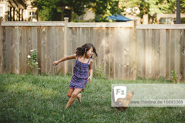 A happy child plays barefoot with a chicken in her backyard garden
