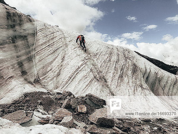 Bergsteiger klettert an einer Eiswand neben einem fließenden Schmelzwasserfluss