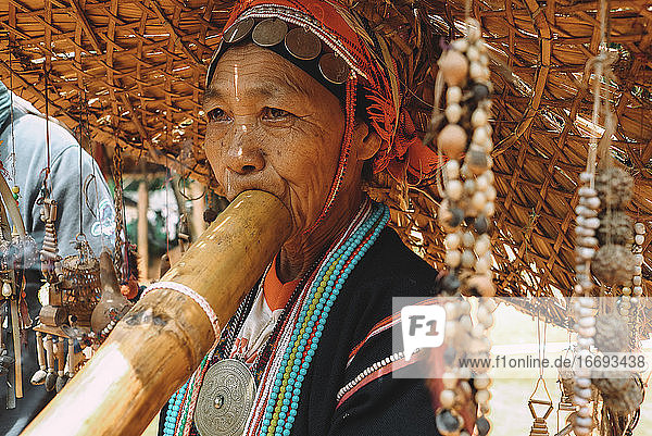 Porträt einer Frau aus einem thailändischen Volksstamm  die ein Musikinstrument spielt.