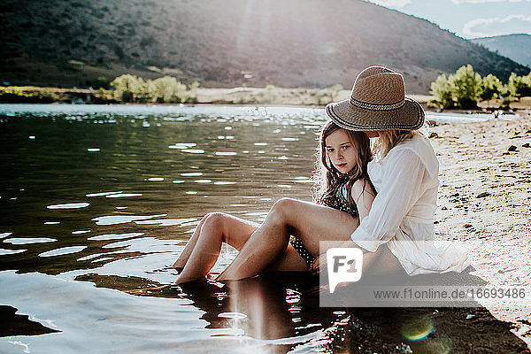 Mutter und Tochter sitzen ruhig im Wasser an einem Seeufer
