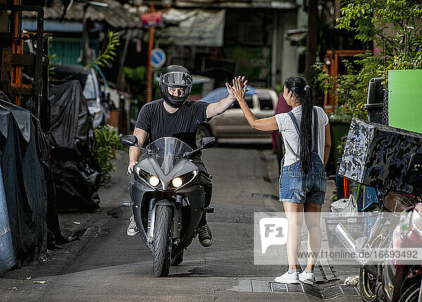 motorcyclist giving a 'high five' to woman in back alley