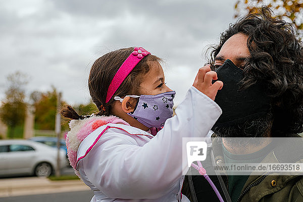 Kleines Mädchen im Halloweenkostüm mit Vater  der eine Schutzmaske trägt