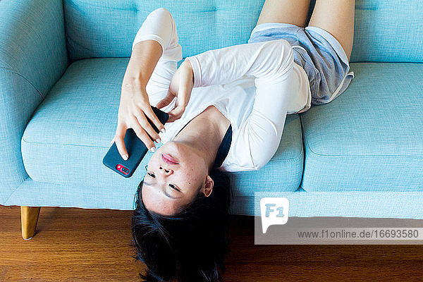 Asiatisches Teenager-Mädchen legt sich hin und benutzt ein Mobiltelefon