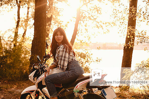 Junge Frau schaut weg  während sie auf einem Motorrad inmitten von Bäumen sitzt