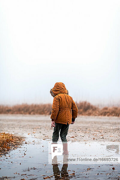 small boy standing in a mud puddle on a gravel road in the fog