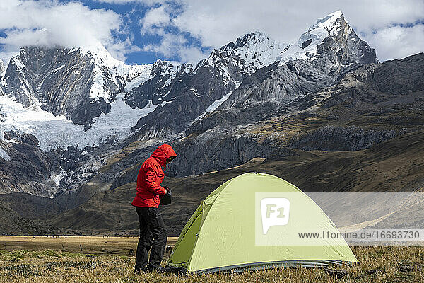 Eine Frau steht in einem Hochgebirgscamp neben einem Zelt in Huayhuash