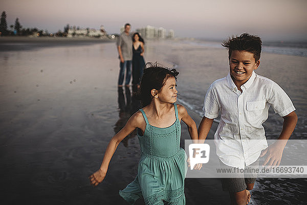 Lachender Junge im Teenageralter und seine Schwester laufen den Eltern am Strand voraus