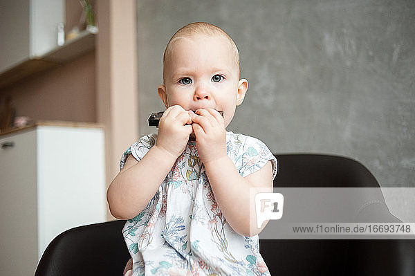Baby girl with short hair close-up plays harmonica at home.