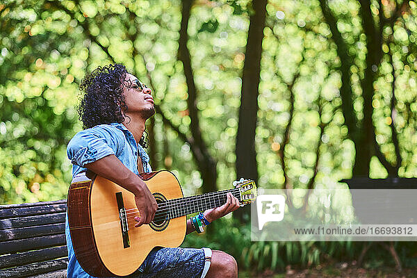 Ein Musiker spielt Gitarre in einem schönen Park. Er ist von Vegetation umgeben.
