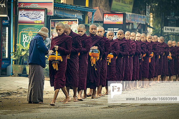 Mönche in einer Warteschlange auf der Straße erhalten Almosen von einem älteren Mann  Nyaung U  Myanmar