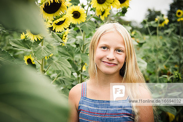 Junges Mädchen in Casual Blue Dress Standing in Sunflower Field Lächelnd