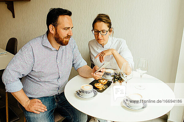 Heterosexuelles Paar im Café  das auf sein Smartphone schaut und Kaffee trinkt