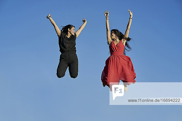 Junge Frauen Paar lächelnd und springen mit blauem Himmel im Hintergrund. Sommer-Konzept