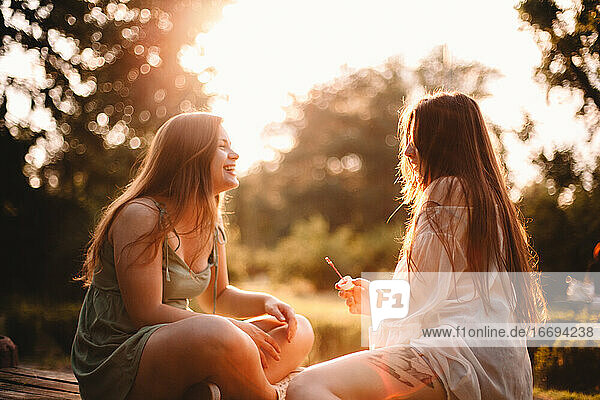 Glückliche Freundinnen sitzen im Sommer bei Sonnenuntergang im Park