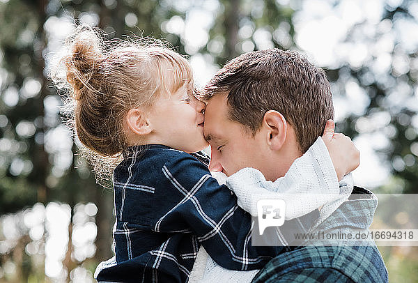 Tochter küsst den Kopf ihres Vaters und sieht zufrieden und glücklich aus