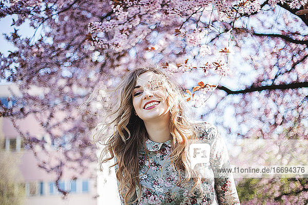 Junge Frau lächelnd vor dem Frühlingsblütenbaum