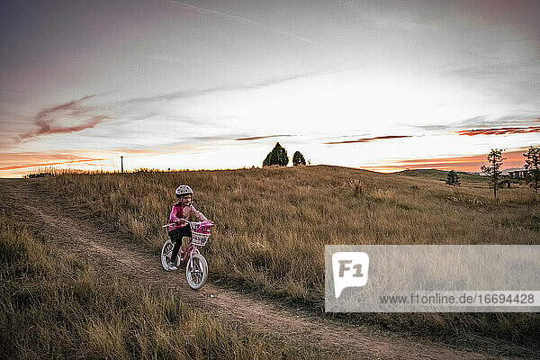young girl bikes down a grassy hill at sunset