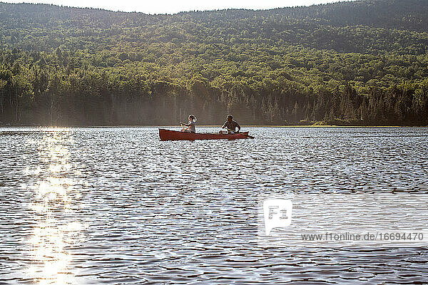 Junger Mann und Frau paddeln mit dem Kanu über einen ruhigen See in den Bergen von Maine