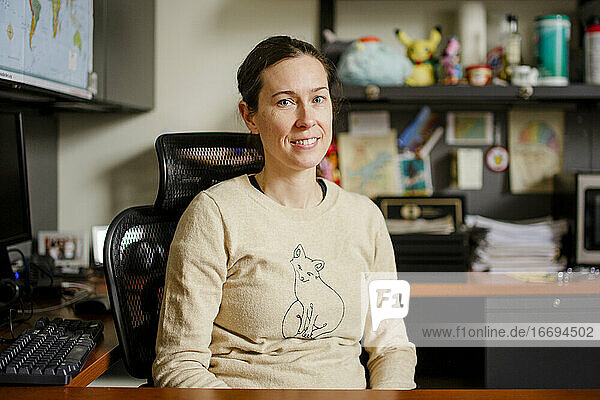 Eine Professorin sitzt in ihrem Büro an einem Schreibtisch und lächelt