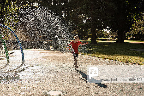 Fröhliches Kind spielt im Wasser in einem Park