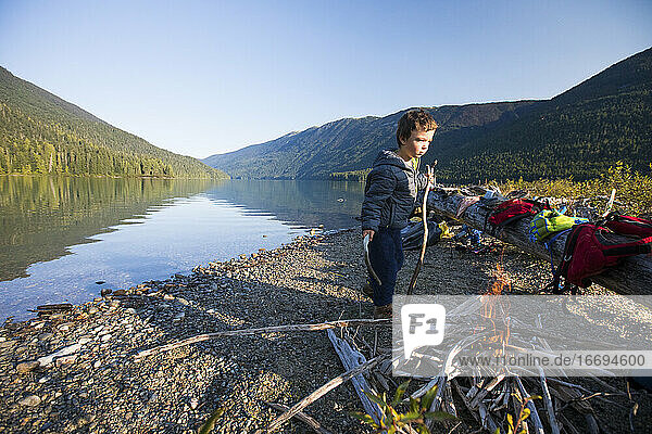 Young boy carries sticks to add to lakeside fire during a camping trip