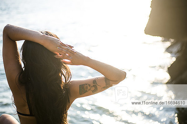 Young Latina Woman relaxing by the ocean at golden hour in summertime