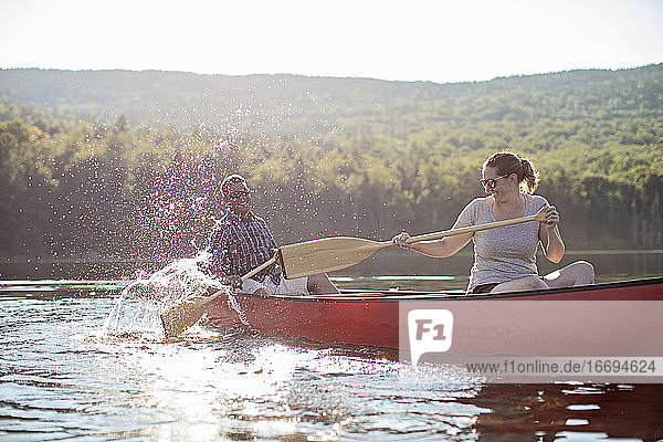 Couple splash each other with canoe paddles while boating on lake
