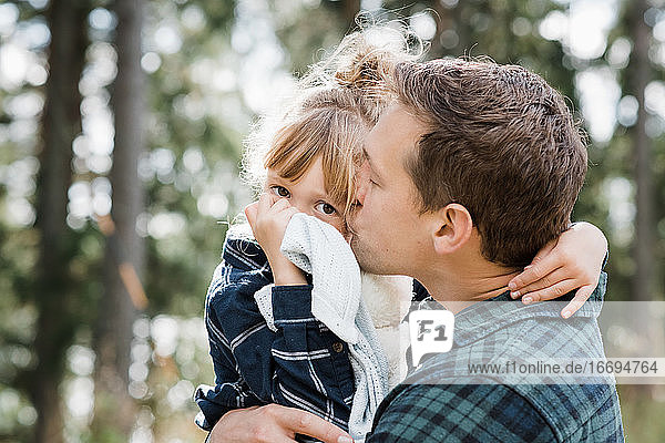 Vater küsst seine Tochter auf die Wange  während sie ihre Decke trägt