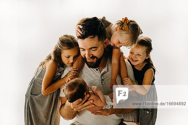 Father and daughters looking at newborn baby sibling and smiling