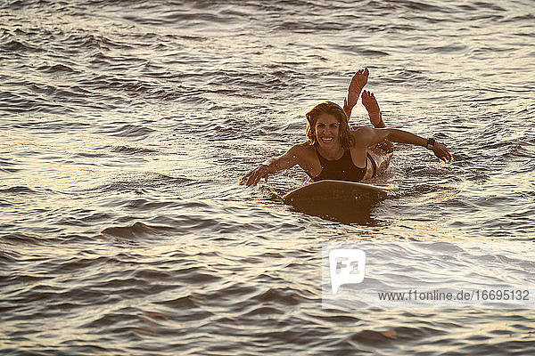 Sportliche Frau paddelt auf Surfbrett bei Sonnenuntergang in Hawaii