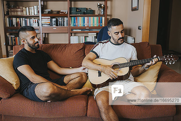 boy plays guitar sitting on the couch his boyfriend