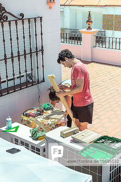 Couple building a piece of furniture on a rooftop on a sunny day.