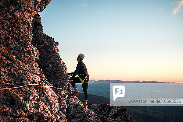 Concept: adventure. Climber woman with helmet and harness. Silhouette at sunset on the mountain. Profile. Resting looking at the climbing route. Via ferrata in the mountains.