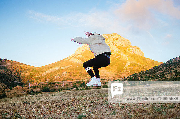 back view of unrecognizable male in casual clothes jumping high against mountains