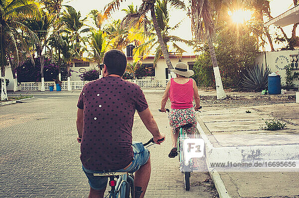 Mann und Frau auf Fahrrädern bei Sonnenuntergang mit Palmen