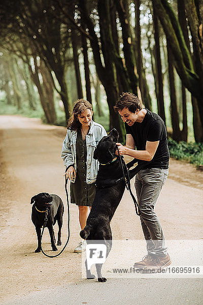 Junges Paar spielt mit zwei Hunden auf einem Waldweg