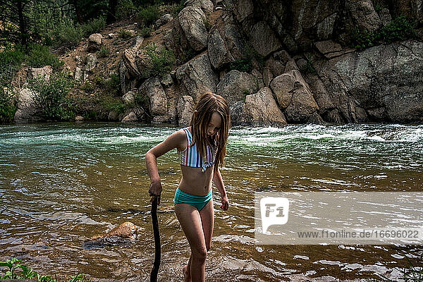 Junges Mädchen spielt mit einem Stock am Ufer eines Flusses