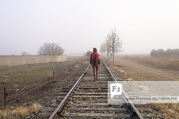 Rückansicht einer Frau mit Kopftuch  die auf einer Bahnstrecke geht