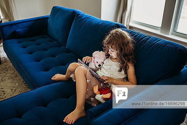 Junges Mädchen sitzt drinnen auf einer blauen Couch und benutzt ein Tablet